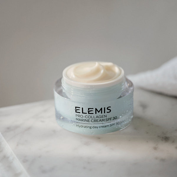 Elemis skincare cream jar on a marble surface with a gray background