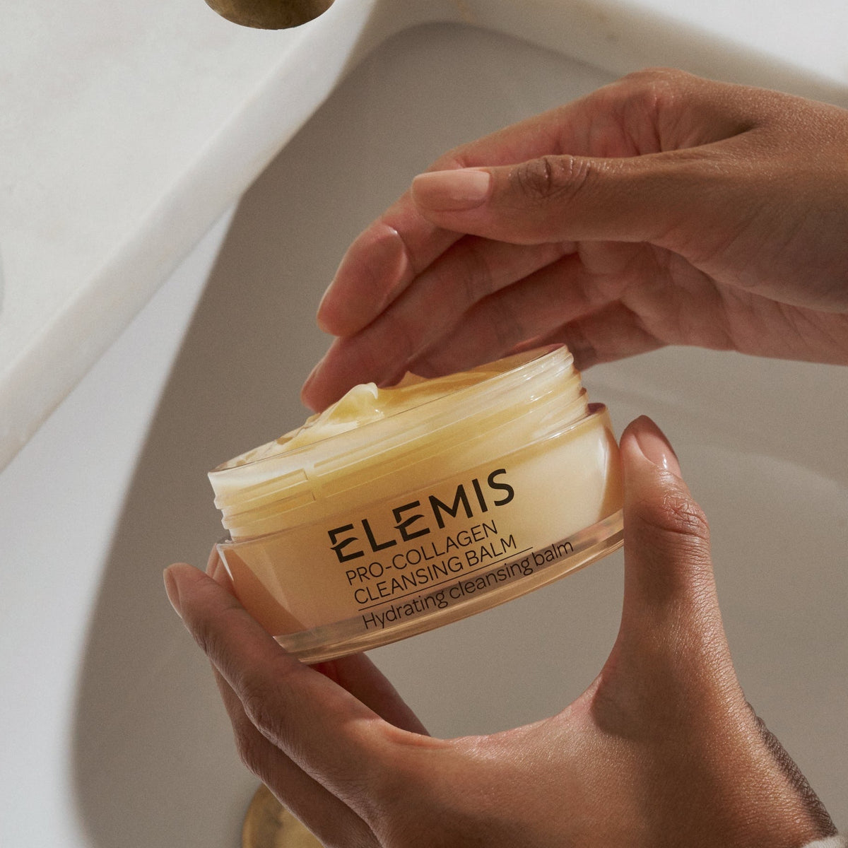 elemis pro-collagen cleansing balm Person holding a jar of Elemis product over a sink