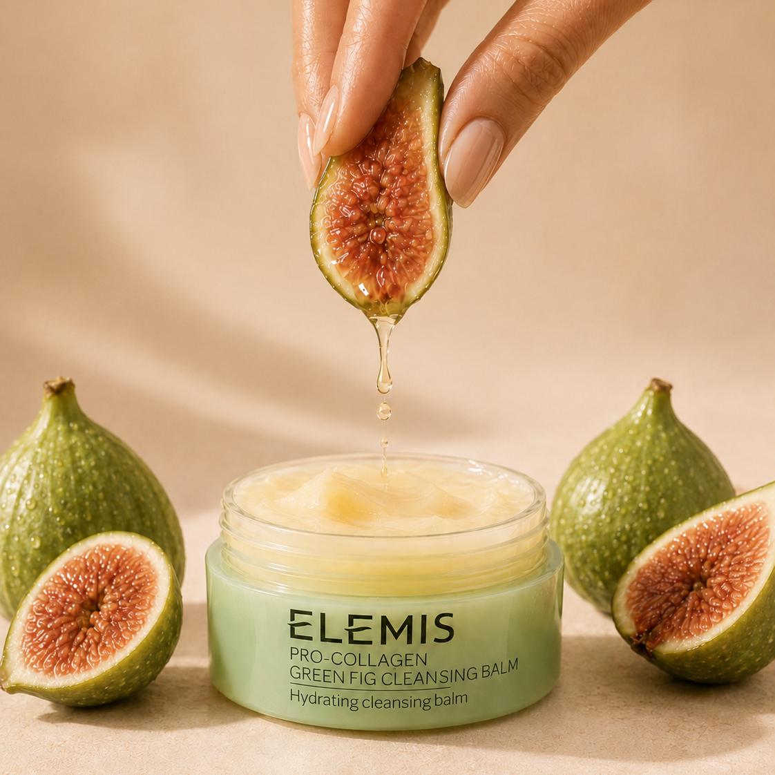 Elemis Green Fig Cleansing Balm in a light green jar, with a hand holding a sliced fig above it as honey drips into the balm. More whole and sliced figs are arranged around the jar on a warm beige background.
